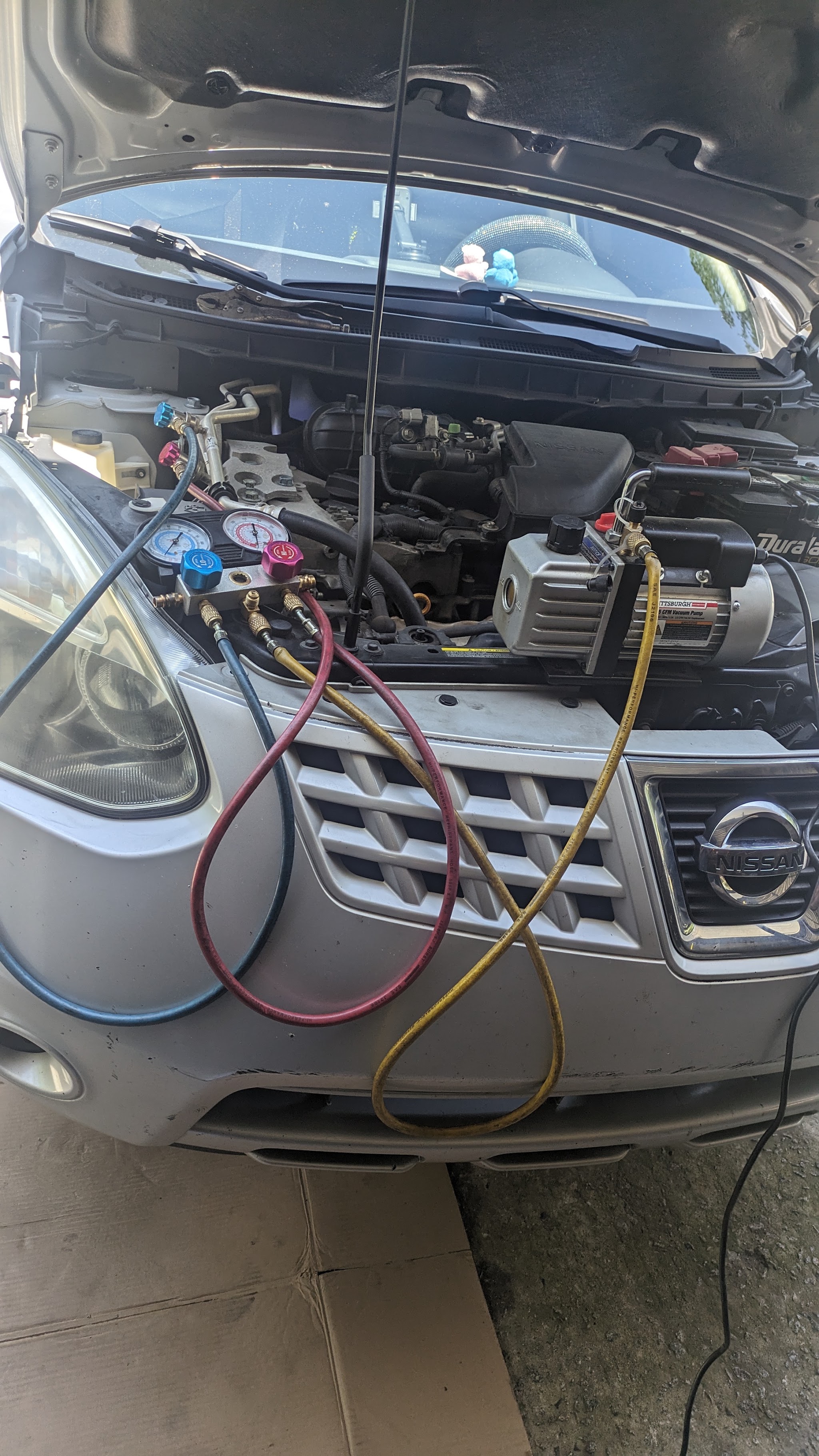 AC service in progress with gauges and a vacuum pump on a Nissan